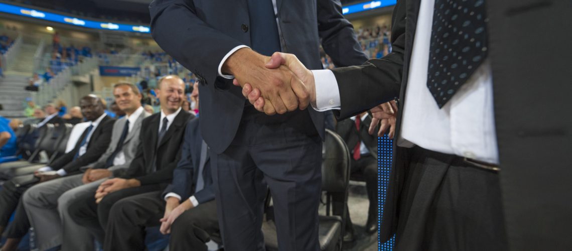 Mid section of businessmen shaking hands in basketball stadium, Arena Stozice, Ljubljana, Slovenia.