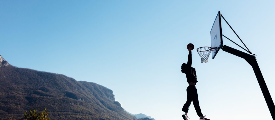 Basketball player jumping and placing ball in the hoop, outdoor basketball court